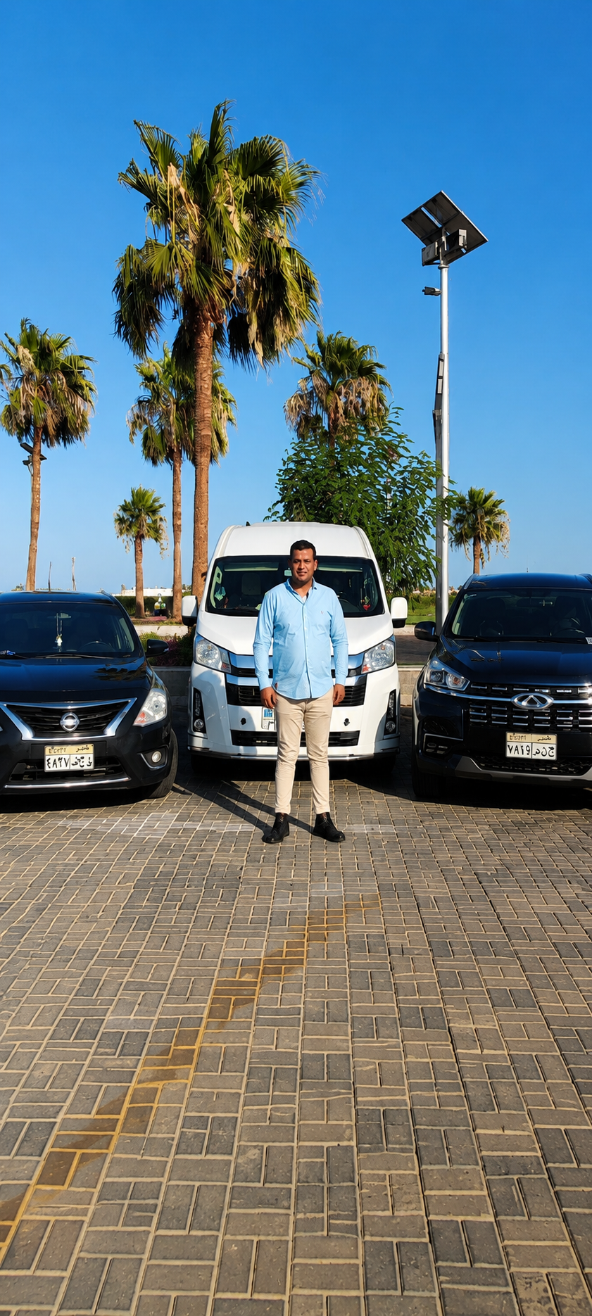 Mohamed Ramadan standing between his transfer van and SUVs under palm trees in South Sinai